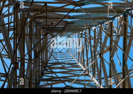 Regarder vers le haut à travers le réseau métallique d'un pylône d'électricité haute tension contre un ciel bleu Banque D'Images