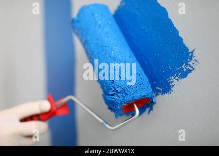 Main tient le rouleau et le fil sur le mur avec de la peinture bleue Banque D'Images