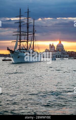Trois voiliers à voile à mâts, MV Sea Cloud ll, quittant Venise, Italie, sous un coucher de soleil chaud, avec la basilique Santa Maria della Salute en arrière-plan Banque D'Images