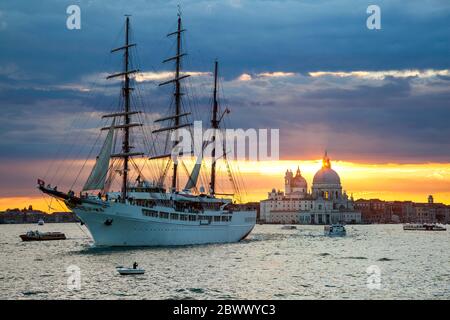 Trois voiliers à voile à mâts, MV Sea Cloud ll, quittant Venise, Italie, sous un coucher de soleil chaud, avec la basilique Santa Maria della Salute en arrière-plan Banque D'Images