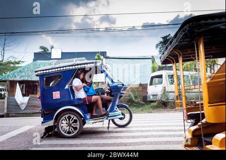 Le célèbre tricycle philippin ou tuk tuk (parfois appelé pousse-pousse) fait son chemin le long de la route principale très fréquentée allant dans Coron Town propre. Île Coron. Banque D'Images