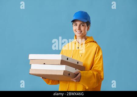 Portrait de la jeune femme en uniforme tenant une pizza et souriant à l'appareil photo sur fond bleu Banque D'Images
