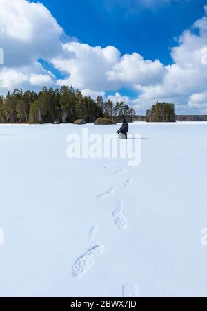 Un homme âgé pêchant sur glace dans un lac forestier à Winter, Finlande Banque D'Images