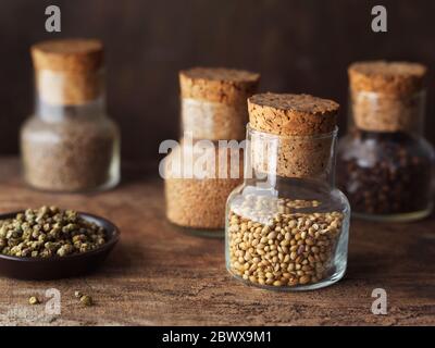 Pots d'épices (graines de coriandre, clous de girofle, graines de moutarde et graines de cumin) et grains de poivre vert dans un petit plat sur table en bois. Banque D'Images