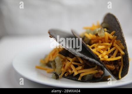 Tacos au maïs bleu coquille dure classique avec bœuf haché et fromage sur plaque blanche vue latérale à proximité Banque D'Images