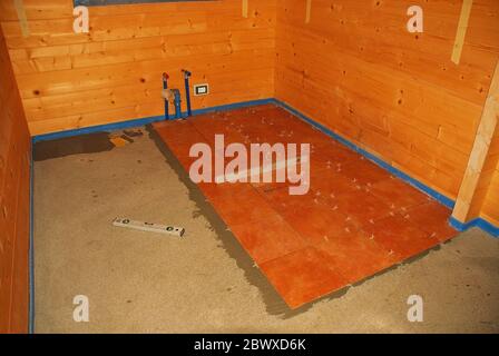 Plancher en béton dans une nouvelle maison en bois (sapin). L'adhésif pour carrelage a été appliqué et les carreaux de sol ont été posés. La mousse bleue protège les murs en bois Banque D'Images