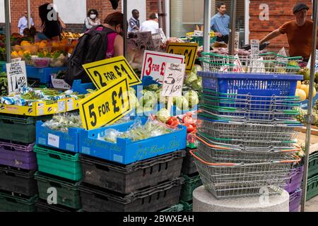 Un marché extérieur de fruits et légumes stalle avec des signes annonçant de bonnes offres et une pile de panier à main à l'avant. Banque D'Images