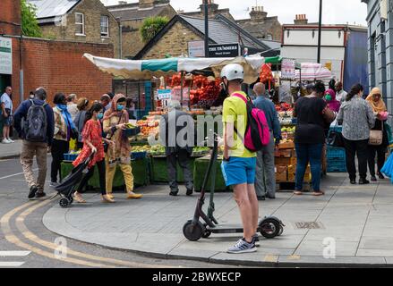 Un marché de fruits et légumes en plein air avec de nombreux clients avides et un homme attendant devant avec un scooter électrique qui sont illégaux en public. Banque D'Images