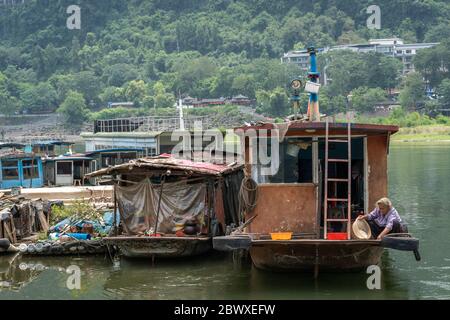 Yangshuo, Chine - août 2019 : femme chinoise vivant dans un bateau amarré sur le rivage de la rivière Li, utilisant un bol en plastique pour le lavage et la lessive Banque D'Images