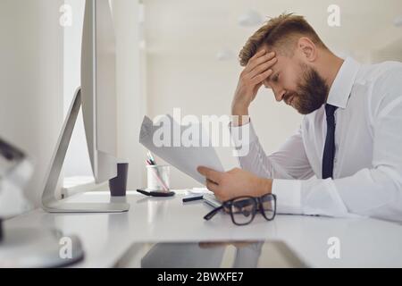 Un homme d'affaires très occupé lit les documents de travail assis à une table avec un ordinateur au bureau. Banque D'Images