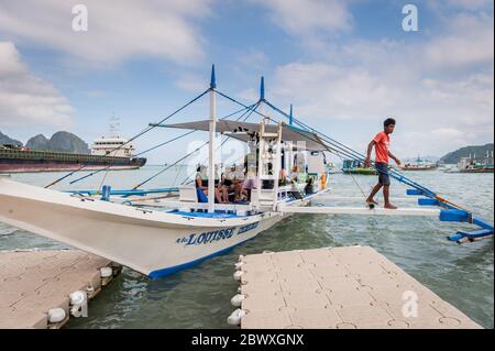 Un bateau à longue queue de pêcheur se charge de fournitures et de touristes pour partir en excursion d'une journée avec un énorme pétrolier derrière à l'île El Nido Philippines. Banque D'Images