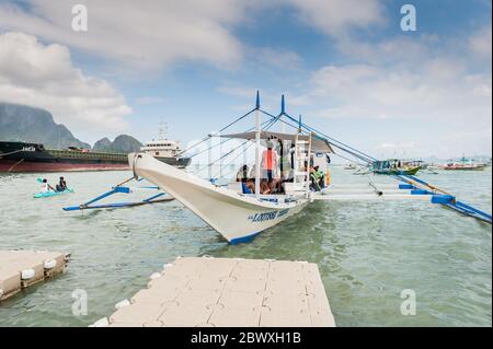 Un bateau à longue queue de pêcheur se charge de fournitures et de touristes pour partir en excursion d'une journée avec un énorme pétrolier derrière à l'île El Nido Philippines. Banque D'Images