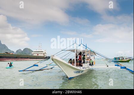 Un bateau à longue queue de pêcheur se charge de fournitures et de touristes pour partir en excursion d'une journée avec un énorme pétrolier derrière à l'île El Nido Philippines. Banque D'Images