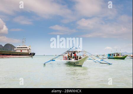 Un bateau à longue queue de pêcheur se charge de fournitures et de touristes pour partir en excursion d'une journée avec un énorme pétrolier derrière à l'île El Nido Philippines. Banque D'Images