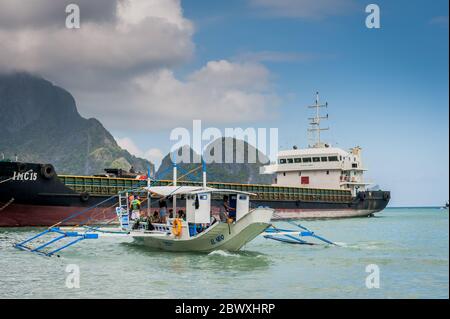 Un bateau à longue queue de pêcheur se charge de fournitures et de touristes pour partir en excursion d'une journée avec un énorme pétrolier derrière à l'île El Nido Philippines. Banque D'Images