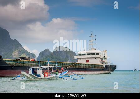 Un bateau à longue queue de pêcheur se charge de fournitures et de touristes pour partir en excursion d'une journée avec un énorme pétrolier derrière à l'île El Nido Philippines. Banque D'Images