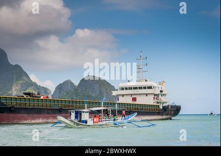 Un bateau à longue queue de pêcheur se charge de fournitures et de touristes pour partir en excursion d'une journée avec un énorme pétrolier derrière à l'île El Nido Philippines. Banque D'Images