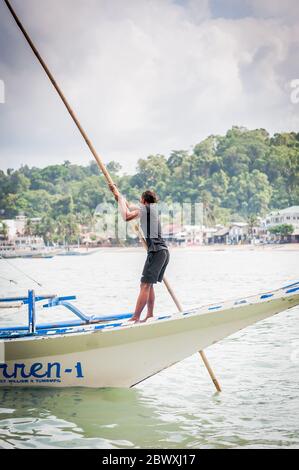 Un capitaine philippin dirige son bateau plein de touristes hors du port pour visiter les îles locales à El Nido, Palawan, Philippines. Banque D'Images