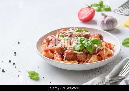 Pâtes fetuccine avec boulettes de viande, parmesan, tomates, basilic dans un bol sur table blanche. Gros plan. Espace pour le texte. Cuisine italienne. Banque D'Images