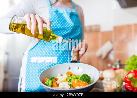 Femme versant de l'huile d'olive sur des légumes dans une casserole à la maison. Concept de repas sain. Banque D'Images