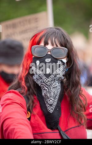 Femme avec une traînée rouge dans ses cheveux et portant des lunettes de soleil et une écharpe protectrice couvrant son visage, Londres, Angleterre, Royaume-Uni Banque D'Images