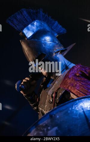 Légionnaire romain en armure avec une épée et un bouclier sur fond noir. Le visage est caché par un casque. Banque D'Images