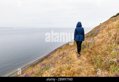 Une jeune femme seule à capuchon sur Ebby Bluff, réserve historique nationale Ebey's Landing, île Whidbey, Washington, États-Unis. Banque D'Images