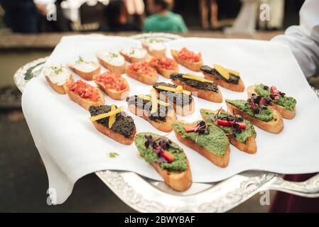 Homme portant un plateau avec divers mini sandwiches. Petits en-cas savoureux. Concept de célébration, fête, anniversaire ou mariage. Banque D'Images