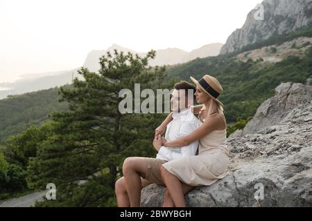 Jeune couple amoureux assis sur le rocher le soir, beau crépuscule. Banque D'Images