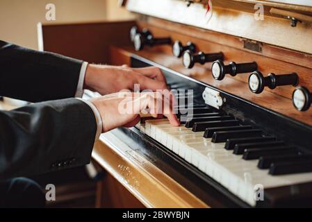 Gros plan sur les mains masculines en costume jouant à l'orgue de pipe dans l'église. Instrument de musique classique vintage. Banque D'Images