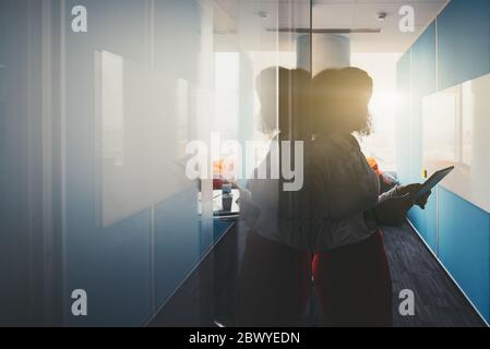 Silhouette d'une femme d'affaires avec une tablette pc entre ses mains à l'entrée d'une salle de conférence de bureau moderne ou d'une salle de réunion avec des murs de BL classique Banque D'Images