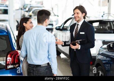 Vendeur proposant une voiture de couple debout au bureau Banque D'Images