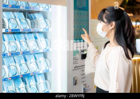 Femme asiatique portant un masque utilisant le masque distributeur automatique pour acheter un masque pour la propagation de la maladie coronavirus Covid-19 dans le centre commercial à Bangkok, Banque D'Images