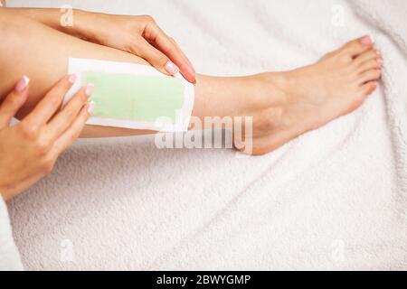 La femme utilise du ruban de cire pour enlever les cheveux sur les jambes Banque D'Images