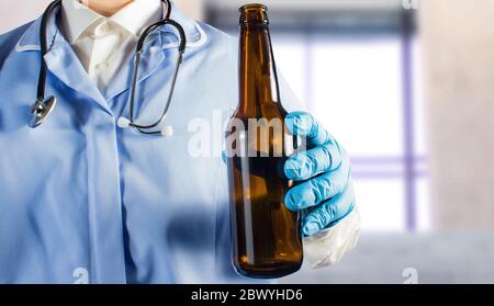 Photo d'un médecin en uniforme avec stéthoscope tenant une bouteille de bière. Banque D'Images