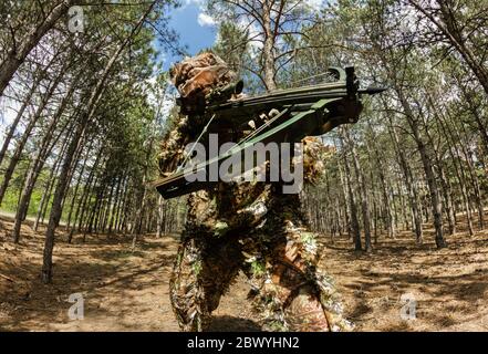 Photo d'un chasseur de sniper de forêt camouflé avec un arc-en-crossbow posé dans les bois. Banque D'Images