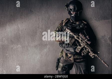Photo d'un soldat entièrement équipé en uniforme de camouflage debout sur fond de mur en béton. Banque D'Images