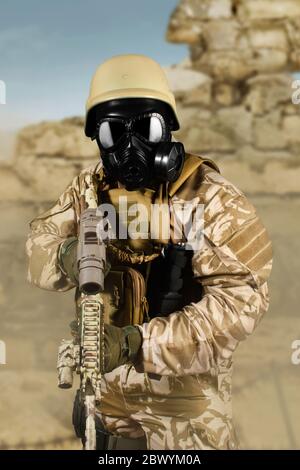 Photo d'un soldat entièrement équipé en uniforme, armure, casque et masque à gaz attaquant avec un fusil en arrière-plan du champ de bataille du désert. Banque D'Images