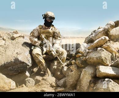 Photo d'un militaire entièrement équipé avec un fusil assis dans une tranchée du désert. Banque D'Images