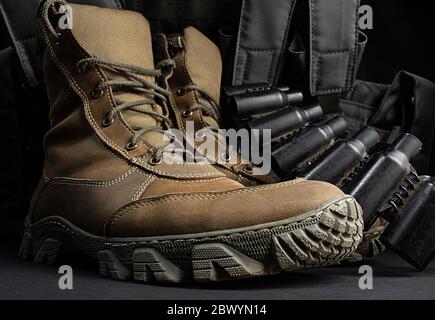 Photo de bottes militaires tactiques en daim marron debout avec gilet d'armure et ceinture à cartouche sur fond noir. Banque D'Images