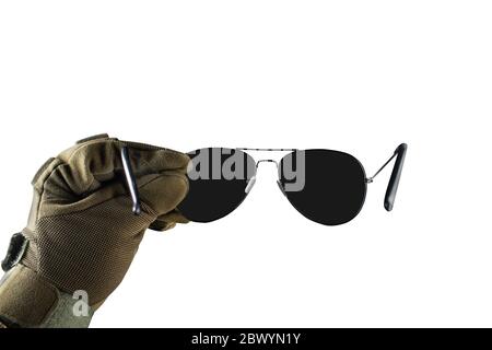 Photo isolée d'un bras de vue de première personne dans une veste tactique et des gants tenant des lunettes de soleil noires sur fond blanc. Banque D'Images