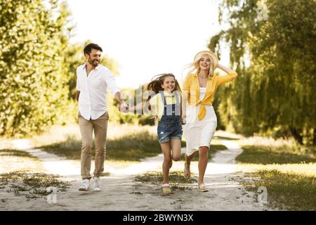 Bonne famille de trois personnes en train de courir en plein air en pleine campagne Banque D'Images