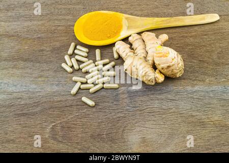 Capsules de plantes de curcuma, racine de curcuma fraîche et poudre de curcuma dans une cuillère en bois sur fond de bois Banque D'Images