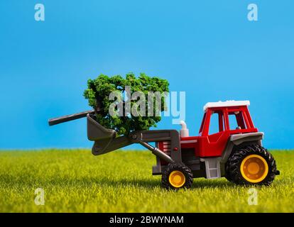 Photo d'un tracktor de jouet debout avec l'arbre sur la surface de l'herbe sur fond bleu. Banque D'Images