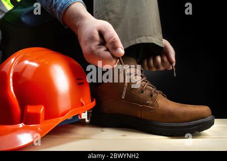 Photo d'un travailleur laçant une chaussure en cuir sur une surface avec un casque de protection. Banque D'Images