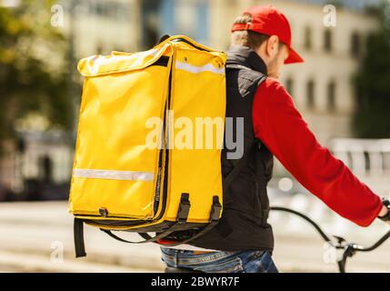 Un messager méconnaissable livrant de la nourriture dans un sac à dos jaune vélo d'équitation à l'extérieur Banque D'Images