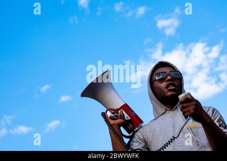 Philadelphie, PA / États-Unis. Une photo à angle bas d'un jeune homme noir portant un sweat à capuche gris et des lunettes de soleil tient un cornet de taureau / haut-parleur isolé sur un fond de ciel bleu et de nuages dispersés. Des centaines de Philadelphiens ont défié le couvre-feu après avoir défilé dans le centre-ville. 03 juin 2020. Crédit : Christopher Evens / Alamy Live News Banque D'Images