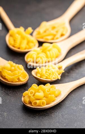 Divers types de pâtes italiennes crues en cuillères en bois sur table noire. Banque D'Images