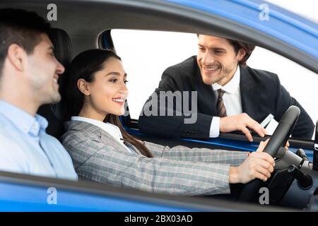 Un couple heureux teste la voiture avec un concessionnaire assis en mode auto Banque D'Images