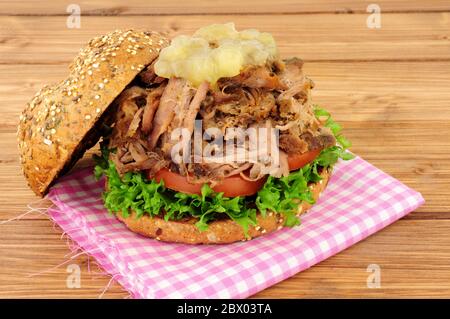 Sandwich au porc rôti de viande avec sauce aux pommes et salade dans un rouleau de pain couvert de graines sur fond de bois Banque D'Images